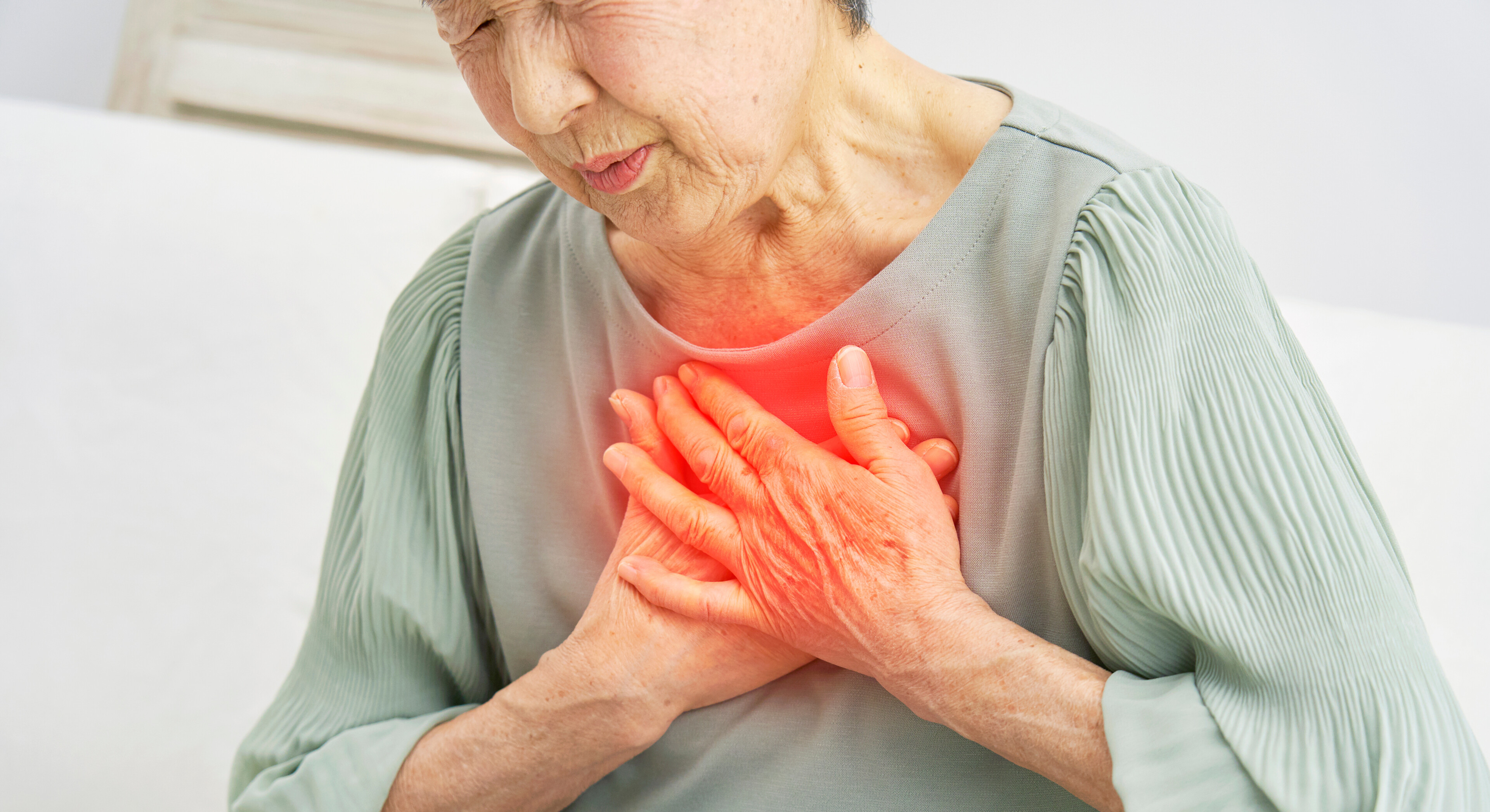 Eine Frau mit Schmerzen sitzt auf einem Sofa und fasst sich auf die Brust. 